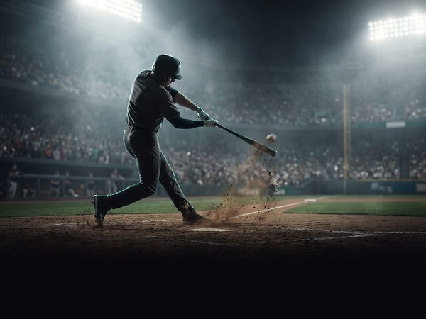 Batter mid-swing at home plate during a night game