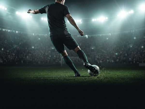 Footballer striking the ball under stadium floodlights